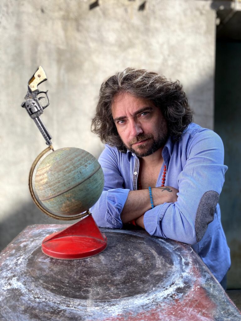 Ritratto a colori di Giulio Cavalli accanto a un mappamondo